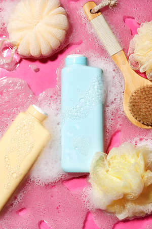Bottles of shower gel and bath supplies into water with foam on color background