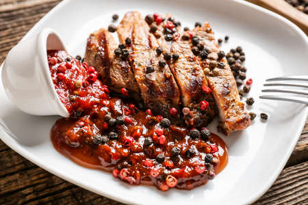 Plate with tasty roasted meat and peppercorn sauce on wooden background, closeupの写真素材