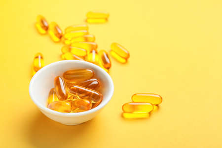 Bowl with fish oil capsules on color backgroundの写真素材