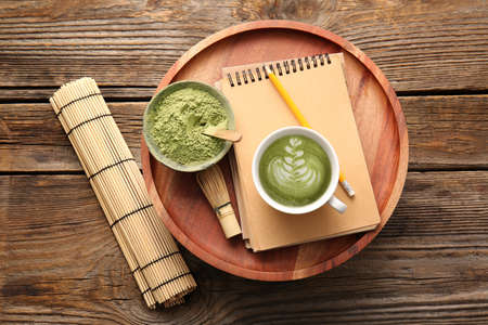 Cup of tasty matcha coffee with powder and notebook on wooden tableの写真素材