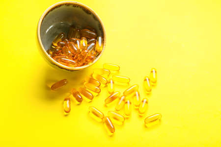 Bowl with fish oil capsules on color backgroundの写真素材