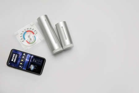 Weather forecast equipment and mobile phone with thermometer on light background with space for text