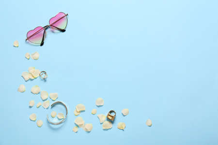 Stylish female jewelry with sunglasses and flower petals on color background