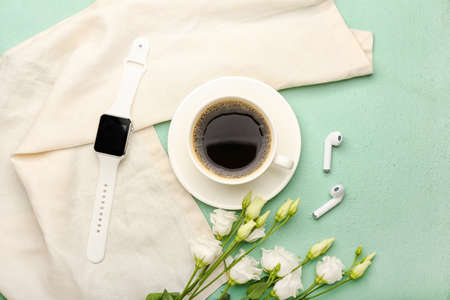 Cup of coffee with flowers and modern gadgets on color background