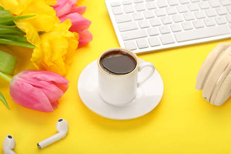 Cup of coffee with flowers and modern devices on color background