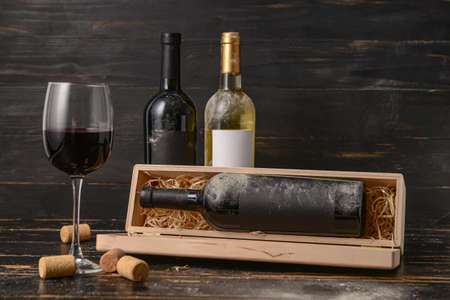 Box with bottles of wine and glass on dark wooden background