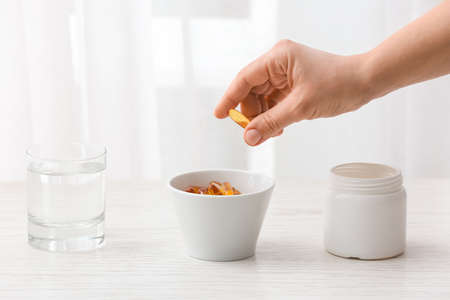 Woman taking fish oil pill from bowl on table, closeup