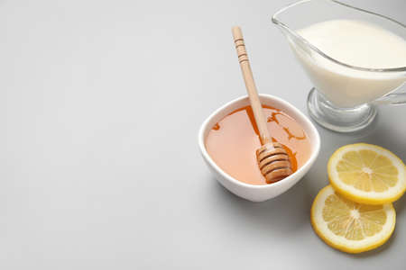 Bowl with sweet honey, lemon slices and jug of milk on gray backgroundの写真素材