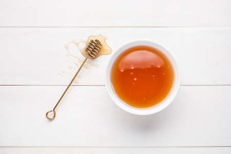 Bowl with sweet honey and dipper on light wooden background