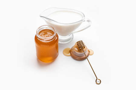 Glass jar with sweet honey, dipper and jug of milk on white backgroundの写真素材