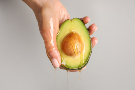Female hand with avocado and dripping honey on gray background, closeup