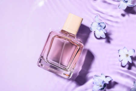Bottle of perfume and flowers in water on color background