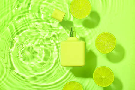 Bottle of perfume and lime in water on color backgroundの写真素材