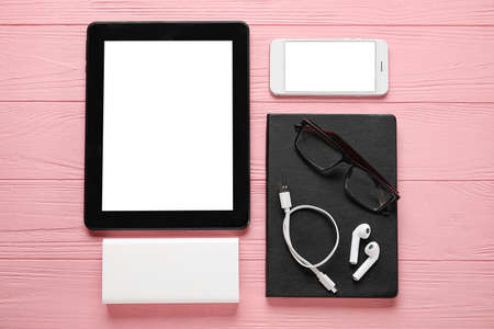 Different modern devices, eyeglasses and notebook on pink wooden background