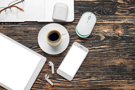 Different modern devices, cup of coffee and eyeglasses on wooden background