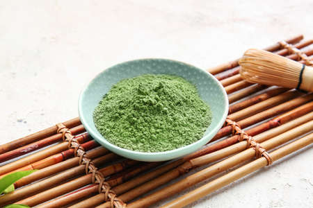 Bowl with powdered matcha tea and chasen on light background