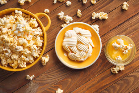 Bowls with tasty popcorn and butter on wooden background