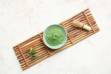 Bowl with powdered matcha tea and chasen on light background