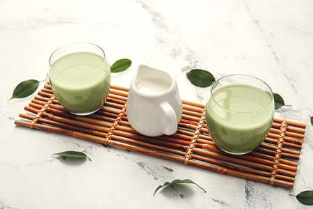 Glasses of matcha tea and milk on light background
