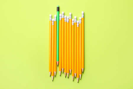 Green pencil among orange ones on color background. Concept of uniqueness