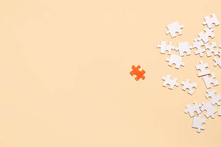 Orange puzzle piece among white ones on color background. Concept of uniquenessの写真素材
