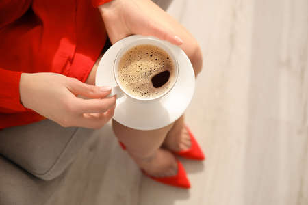 Woman drinking tasty coffee in armchair indoors, closeupの写真素材
