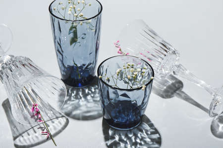 Beautiful empty glasses and flowers on gray background, closeup