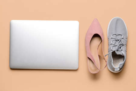 Laptop with high-heeled and sports shoes on color background