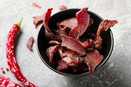 Bowl with spicy beef jerky on grunge backgroundの写真素材