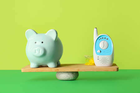 Piggy bank with baby monitor on teeterboard against color background. Concept of balance
