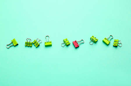 Pink paper clip among green ones on color background. Concept of uniqueness