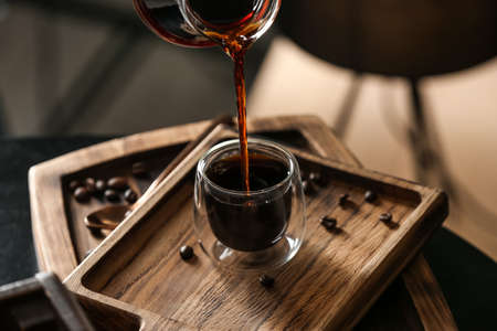 Pouring of hot turkish coffee into glass cup on board