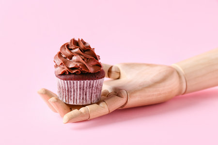 Wooden mannequin hand with tasty chocolate cupcake on color backgroundの写真素材