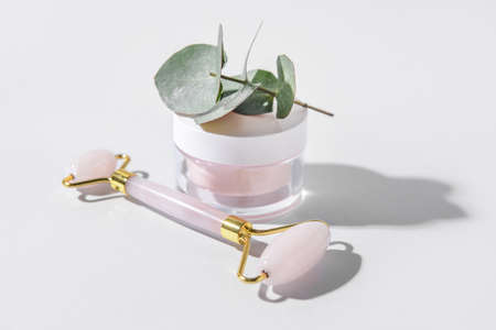 Face massage roller with cosmetic cream on light background