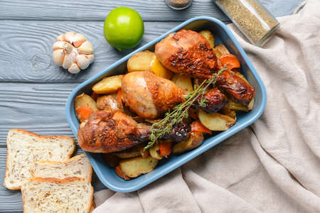 Baking dish with tasty cooked chicken drumsticks and potatoes on tableの写真素材