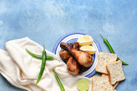 Tasty cooked chicken drumsticks with bread on color backgroundの写真素材