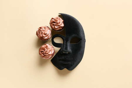 Masquerade mask with tasty chocolate cupcakes on light background
