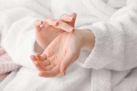 Young woman applying cosmetic cream onto her hands at home, closeup
