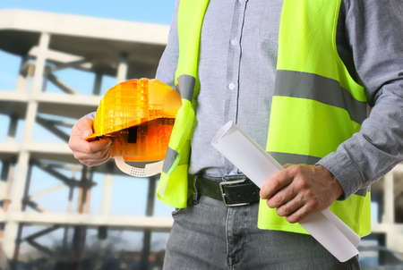 Male worker with safety hardhat and drawing at construction site