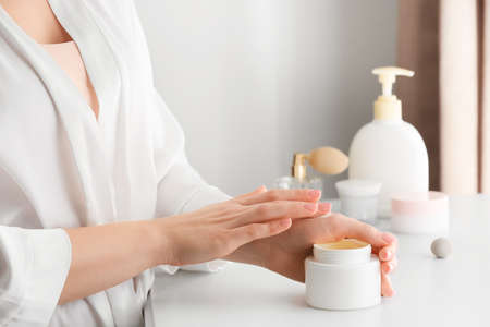 Young woman applying cosmetic cream onto her hands in bathroomの写真素材