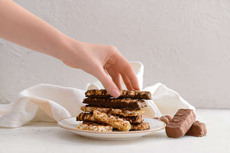 Female hand with tasty chocolate nut bars on plate against light backgroundの写真素材