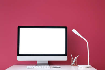 Stylish workplace with modern computer and lamp near color wall