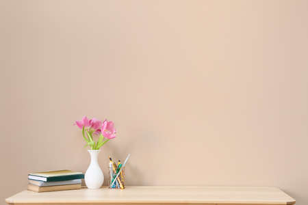 Stylish workplace with beautiful flowers, notebooks and pen holder near color wall