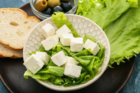 Bowl with delicious pieces of feta cheese and lettuce on plateの写真素材