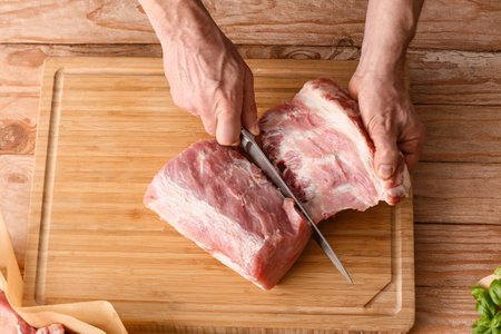 Man cutting raw pork meat on wooden tableの写真素材
