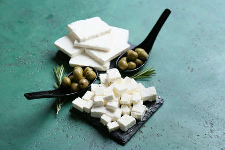 Tasty feta cheese, rosemary and spoons with olives on color backgroundの写真素材