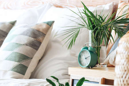 Alarm clock and vase with plant leaves on bedside tableの写真素材