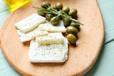 Board with tasty feta cheese, rosemary and olives on color wooden background
