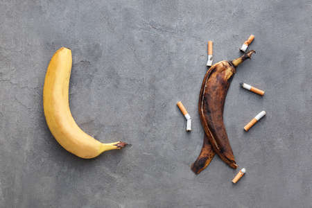 Fresh and rotten banana with cigarettes on grunge background