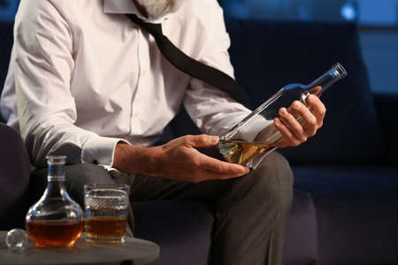 Senior man with bottle of drink late in the evening at homeの写真素材